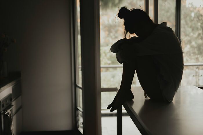 A silhouetted woman sitting alone on a table, conveying a depressing, deep secret.