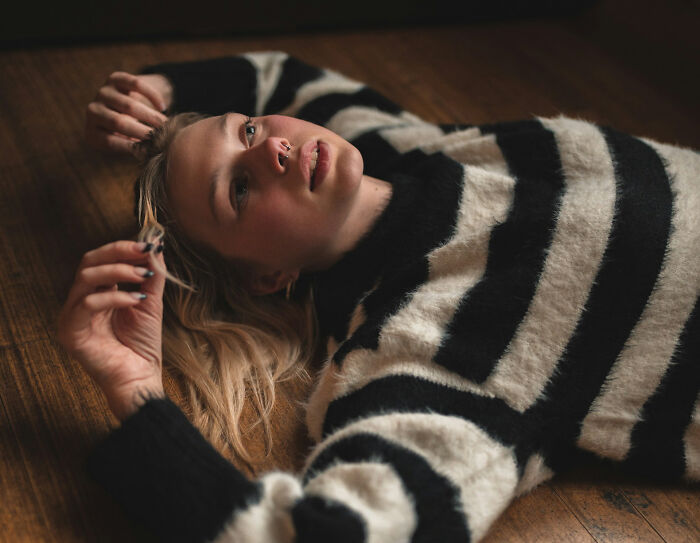 A young woman with blonde hair lying on a wooden floor in a black and white striped sweater, representing unhinged therapist moments.