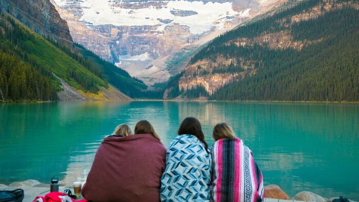 Four people, bundled in blankets, watching the serene turquoise lake and majestic snow-capped mountains. A voice of reason.