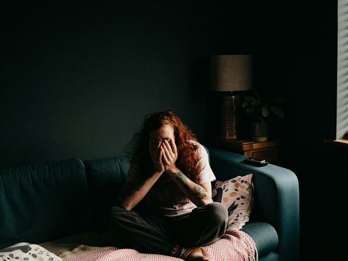 A person with red hair sits on a couch, hands covering their face, sharing their deep secrets.