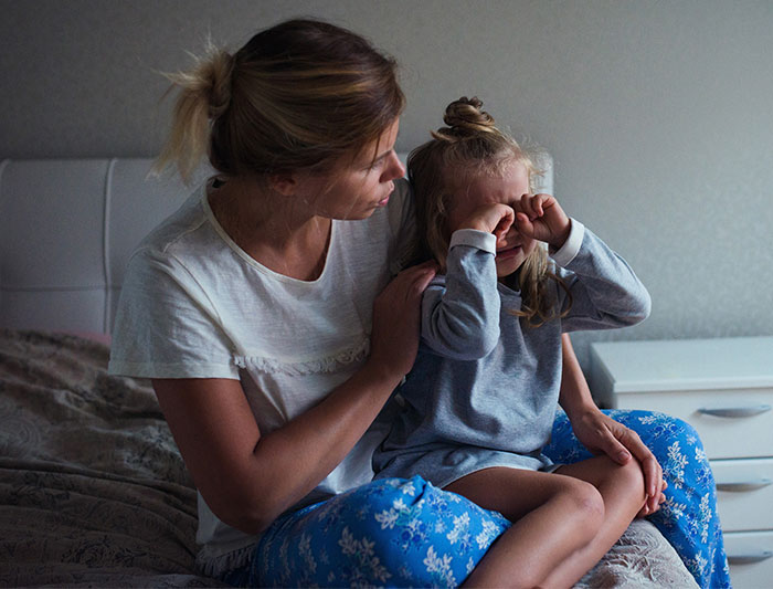 A caring single mom comforts her crying child in bed, as she deals with the struggle of losing a free babysitter. A caring single mom comforts her crying child in bed, as she deals with the struggle of losing a free babysitter.