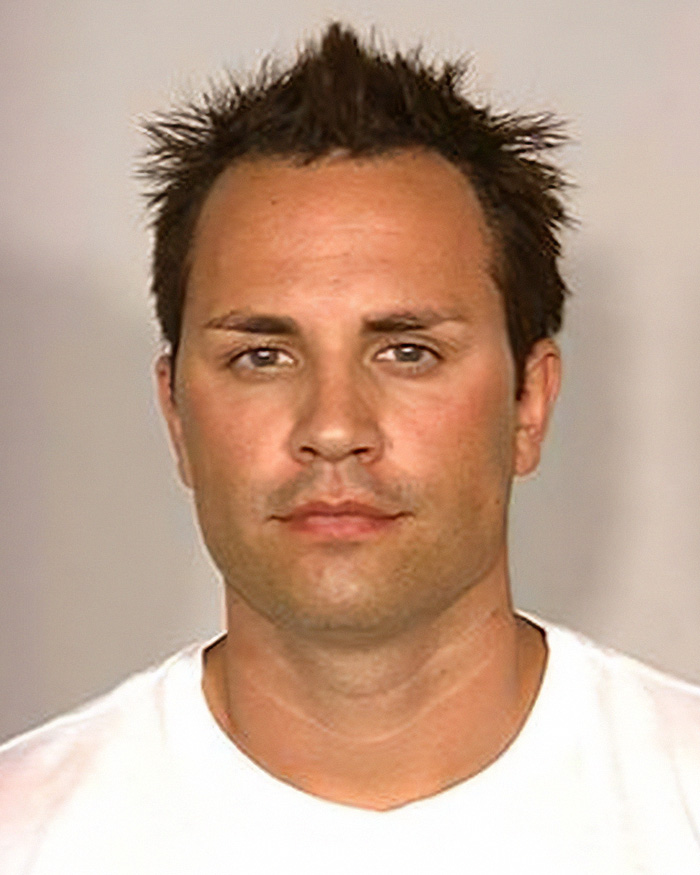 Mugshot of a reality star with spiky hair and a white t-shirt, involved in serious crimes.