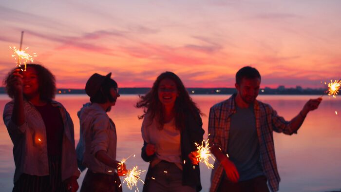 Friends enjoying fireworks by the water at sunset, potentially navigating 'Am I overreacting?' moments.