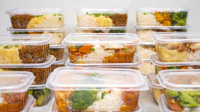 Numerous clear plastic containers filled with various prepared meals, stacked neatly. Red, green, and beige flags.