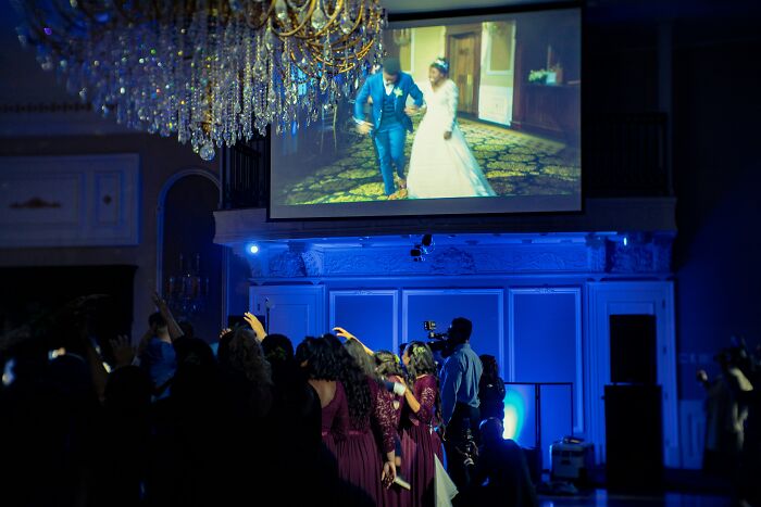 Guests at a wedding watching a video of a bride and groom on a large projection screen.