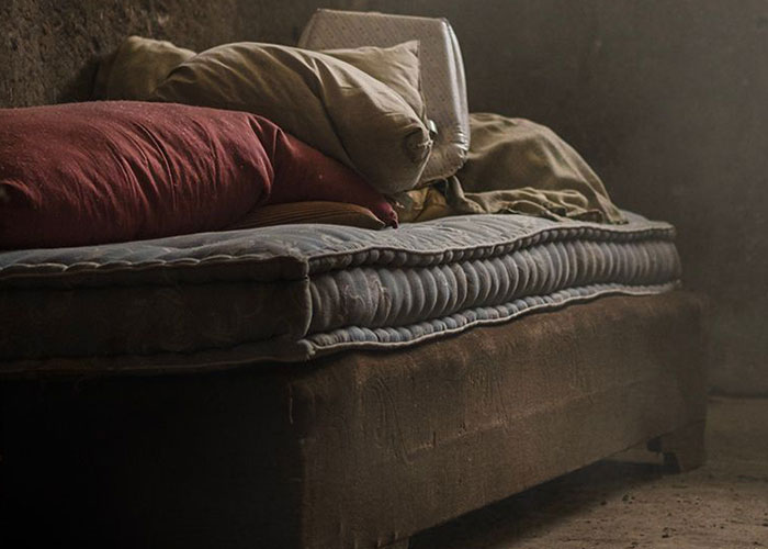 A dirty, old mattress and pillows in a dimly lit room, indicating an unkempt man's home.