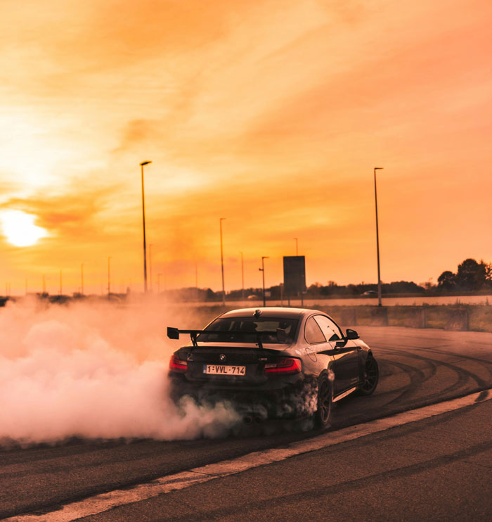 A black sports car drifting, creating a lot of smoke at sunset, symbolizing men's freedom and desire.