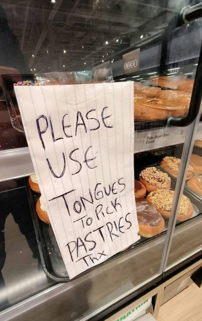 A handwritten sign on a pastry display reads, PLEASE USE TONGUES TO PICK PASTRIES Thx, highlighting cultural decline.