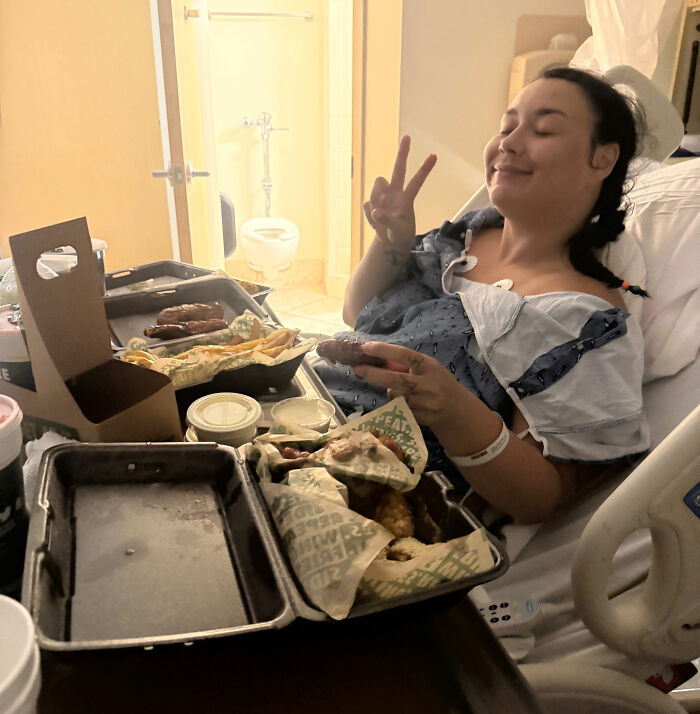 A woman recovering from a catastrophic cruise injury in a hospital bed, eating food and making a peace sign. A woman recovering from a catastrophic cruise injury in a hospital bed, eating food and making a peace sign.