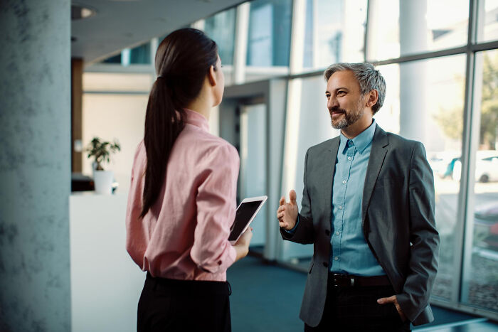 Two workers in a modern office, discussing corporate buzzwords and practices.