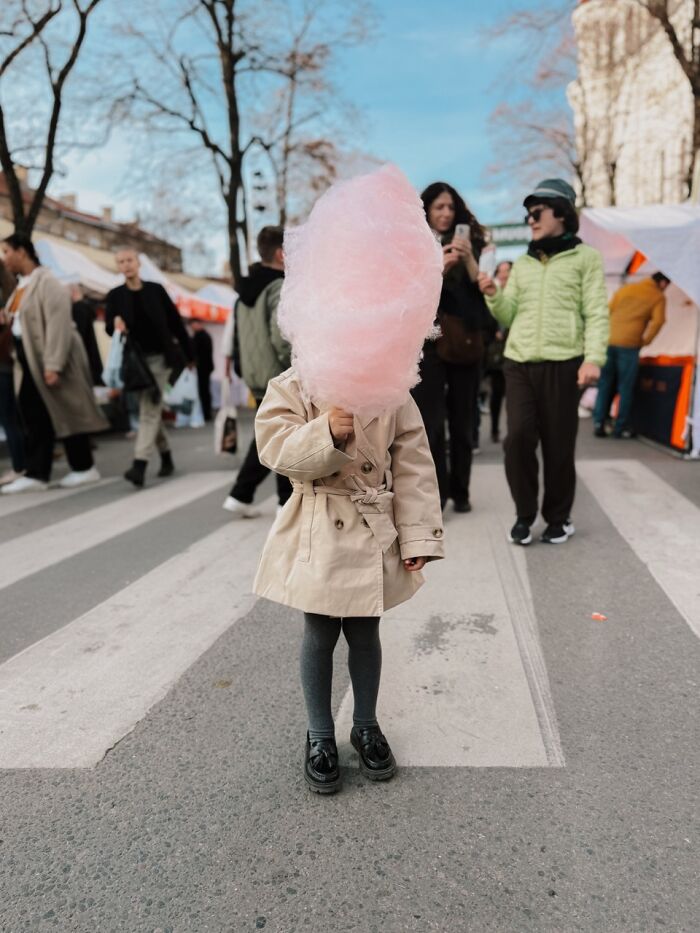 A small child in a trench coat holding pink cotton candy, obscuring their face, a winning iPhone Photography Awards photo.