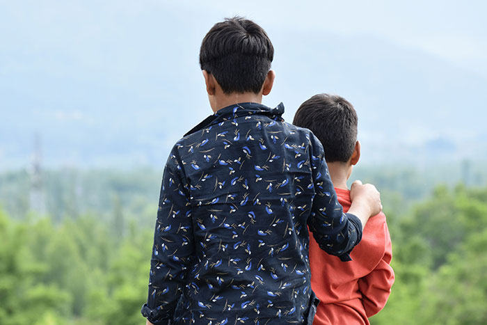 Two kids from behind, one with an arm around the other, contemplating the future and their names.