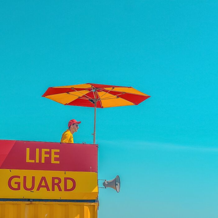 A lifeguard on duty under a red and yellow umbrella, part of the iPhone Photography Awards winning photos.