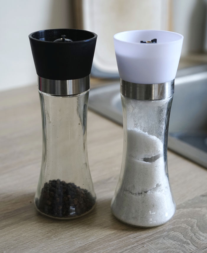 Two glass grinders, one filled with black peppercorns and the other with salt, highlighting surprisingly affordable kitchen essentials.