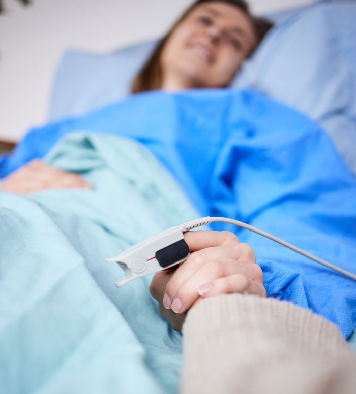 A medical worker holding a patient's hand with a pulse oximeter attached, revealing a hidden side of hospitals.