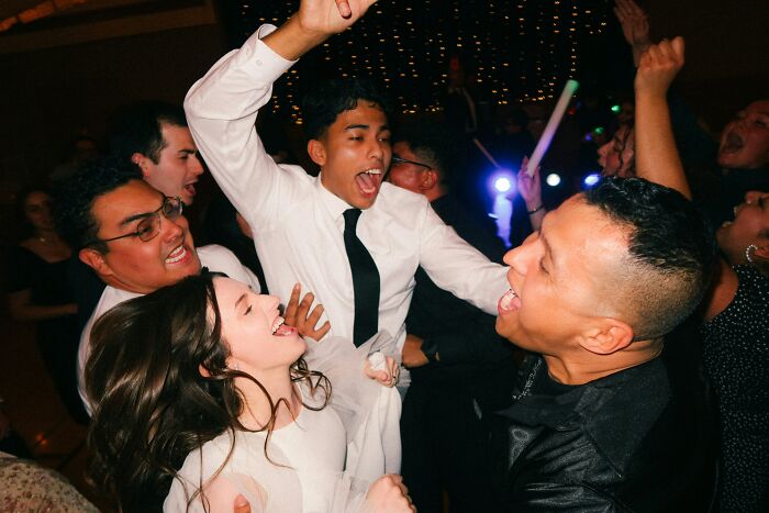 Happy guests celebrating and dancing at a wedding, with one person lifted on another's shoulders.