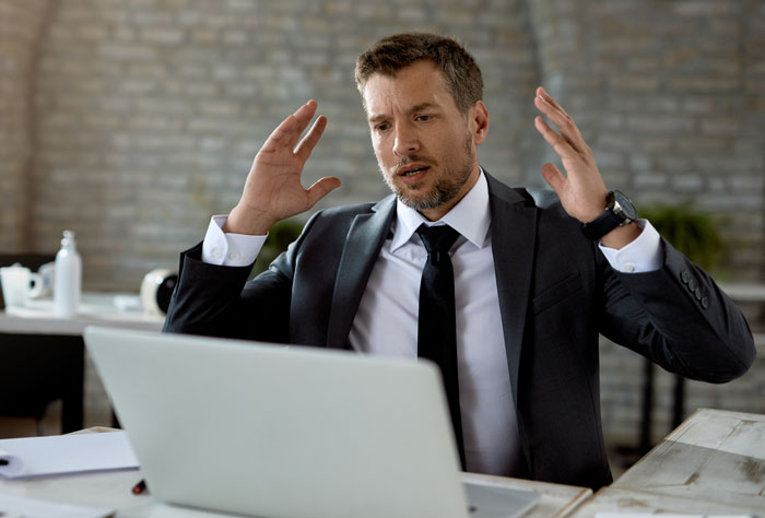 A man in a suit looking frustrated while looking at his laptop, depicting a boss story.