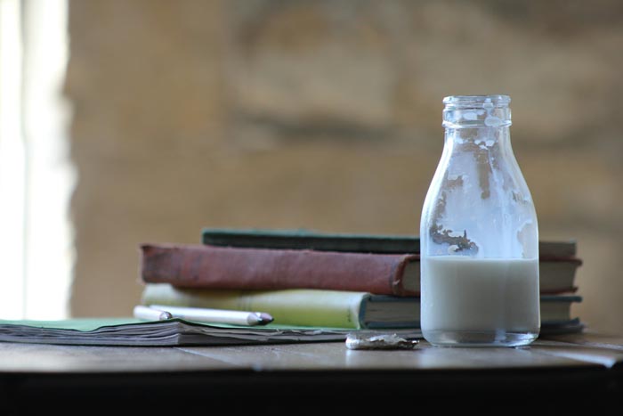 A glass bottle of milk on a table with books, illustrating unhygienic scenarios.