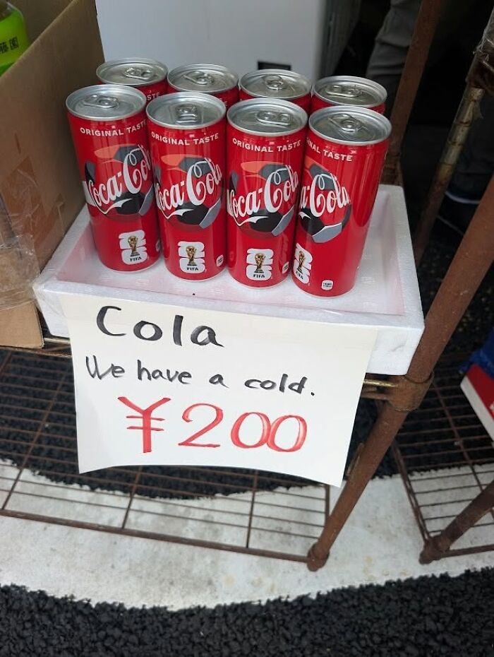 Coca-Cola cans next to a sign that reads Cola We have a cold, an example of getting lost in translation in Japan.