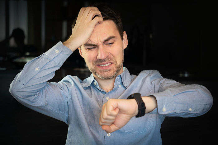 A man looks at his watch with a stressed expression, showcasing dumb reasons people get fired.