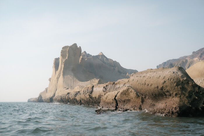 Rugged rock formations rise from the calm waters of the sea, under a clear sky in the Strait of Hormuz.