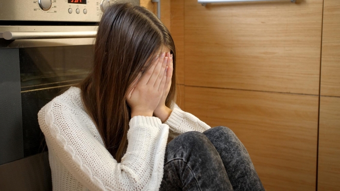 A sad teen sister crying over food during a woman's birthday dinner, covering her face while sitting on the floor.