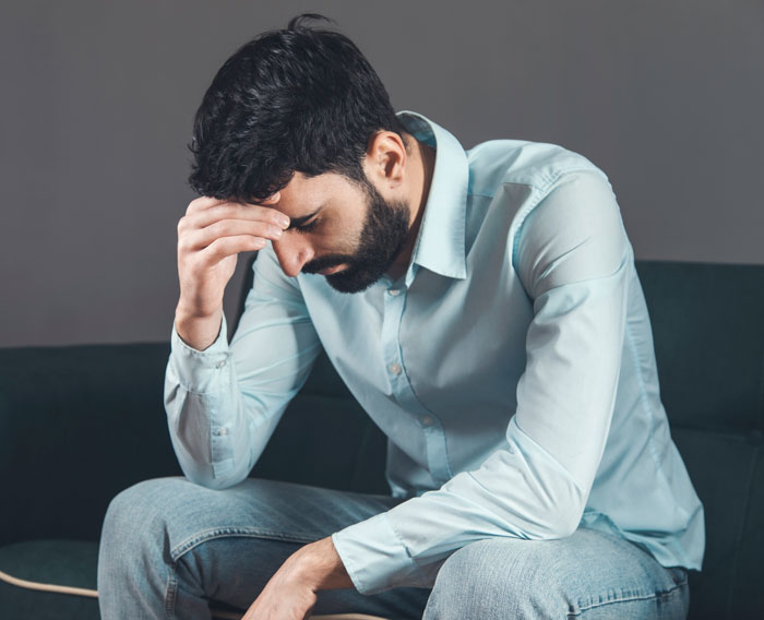 A man sitting with his head in his hand, illustrating the emotional difficulties men face after having a baby.