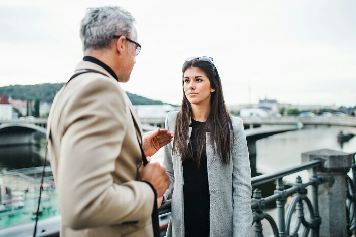 A mature man and younger woman having a serious discussion outdoors, exploring age-gap relationships.