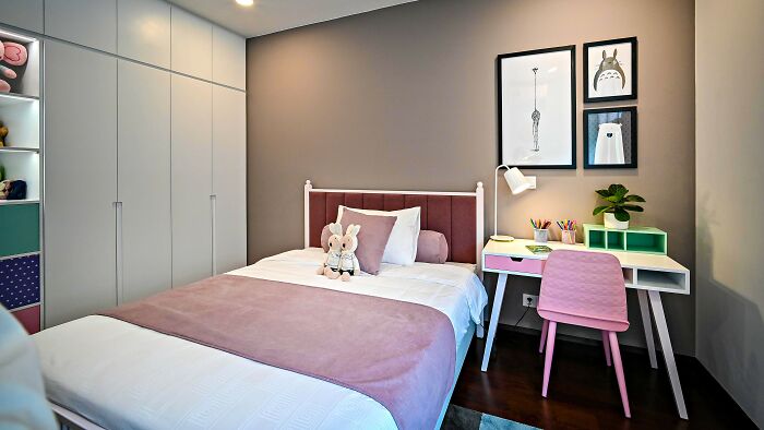 A charming children's bedroom with a pink bed, desk, and decorative frames on the wall.