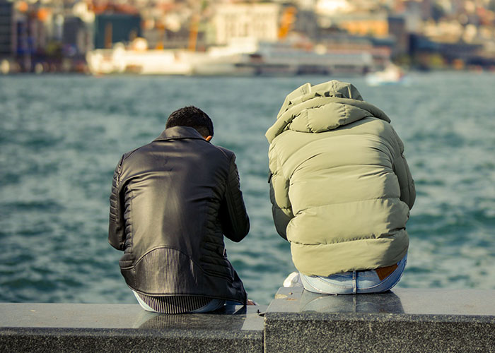 Two people sit by the water, contemplating if reality break is possible.