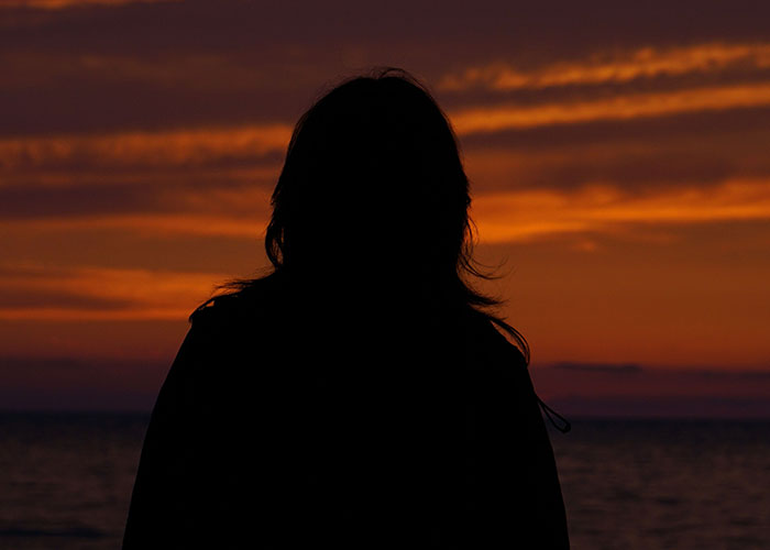 A silhouette of a person facing a dramatic sunset over water, representing the loneliest time. Birthdays can become a source of sadness.