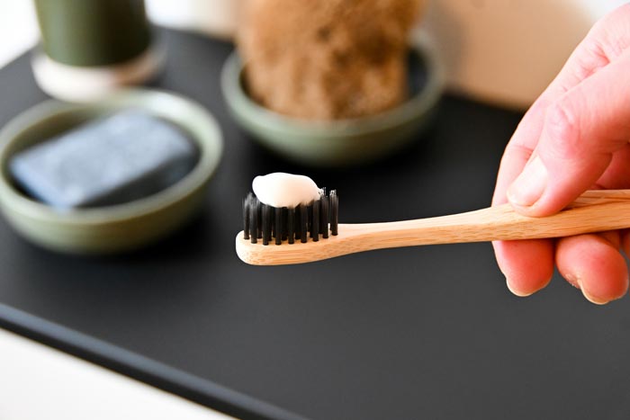 A hand holding a bamboo toothbrush with toothpaste, highlighting unhygienic practices.