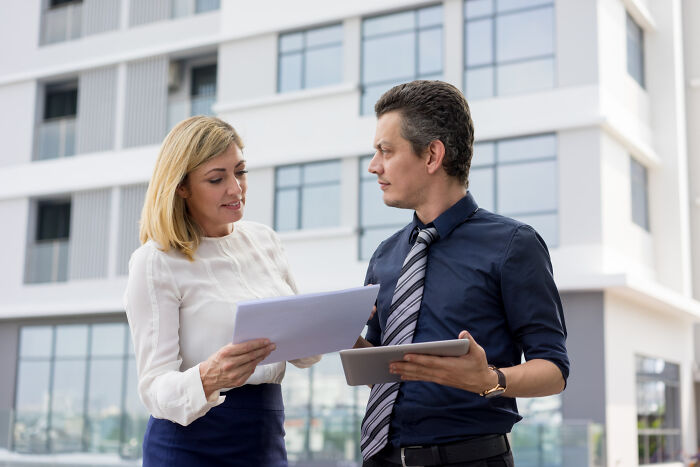 Two coworkers discussing documents outdoors; common reasons people got fired for dumb reasons.