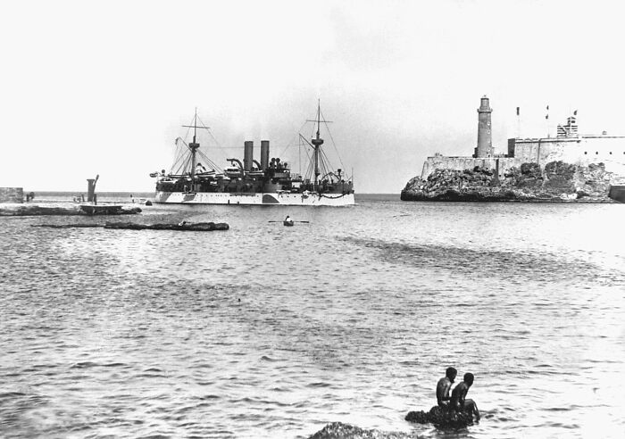 A black and white photo of a ship sailing into a harbor with a lighthouse and fort, revealing intriguing history facts.