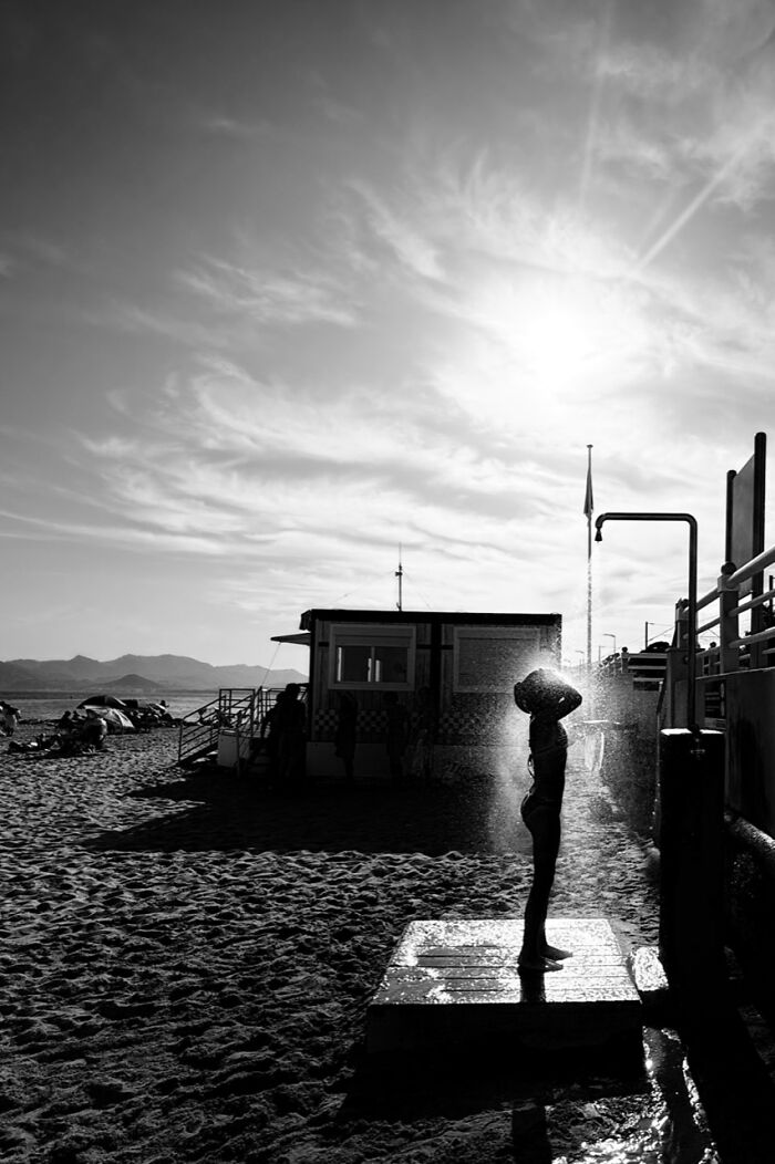 Black and white iPhone Photography Award winning photo of a person showering outdoors on a beach at sunset.