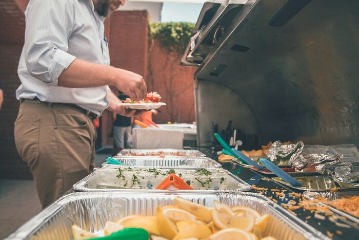 A man serving food at an outdoor wedding event, reflecting on the time and money spent.