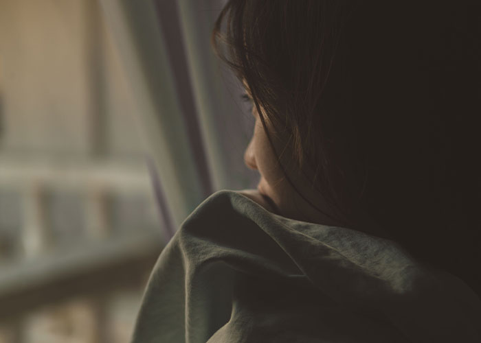 A person looking out a window, feeling the loneliest time. Many people reveal why they no longer look forward to their birthdays.