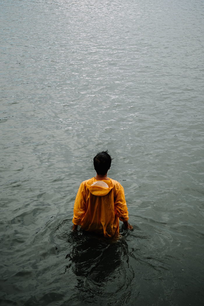 A man in a yellow raincoat stands in dark, mysterious water, with his back to the viewer, hinting at creepy events.