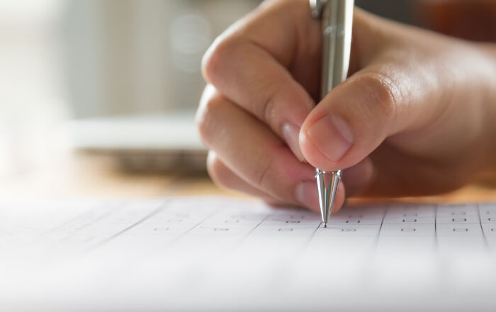 A hand holding a pen, filling out a form, symbolizing corporate practices and paperwork.