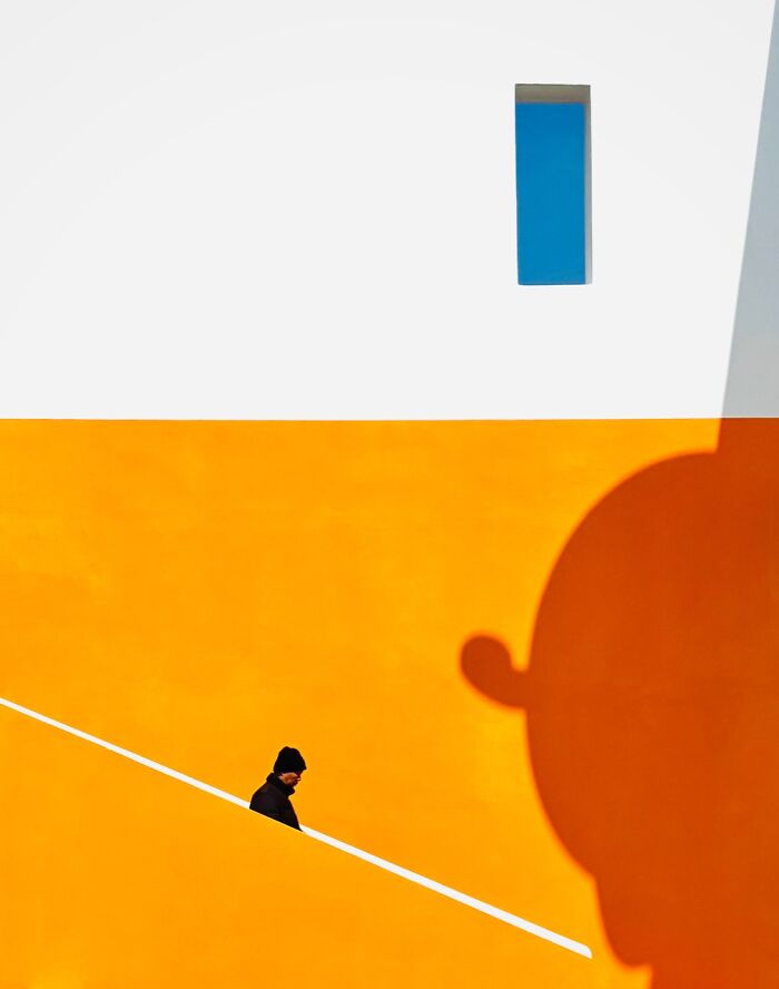 iPhone Photography Award winning photo of a person walking along a yellow wall with a blue window.