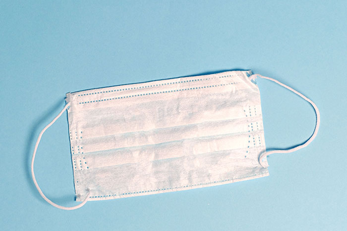 A white surgical mask lies on a light blue background, unrelated to unfortunate names.
