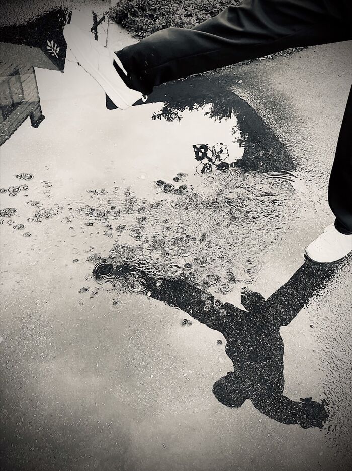 Black and white iPhone Photography Award winning photo of a person stepping into a puddle, creating splashes.