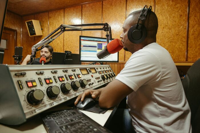 Two men in a radio studio, one speaking into a microphone while wearing headphones, showing an unexpected situation for people got fired from their jobs.