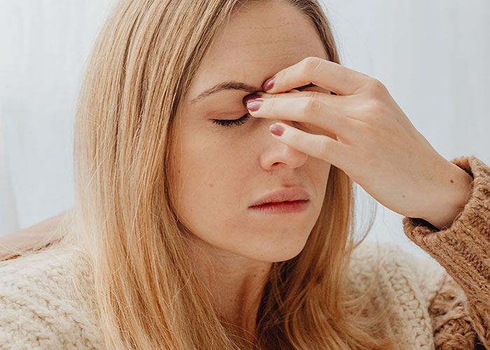 A woman with her eyes closed, pressing her fingers to her forehead, reflecting women taking an Epi Pen.