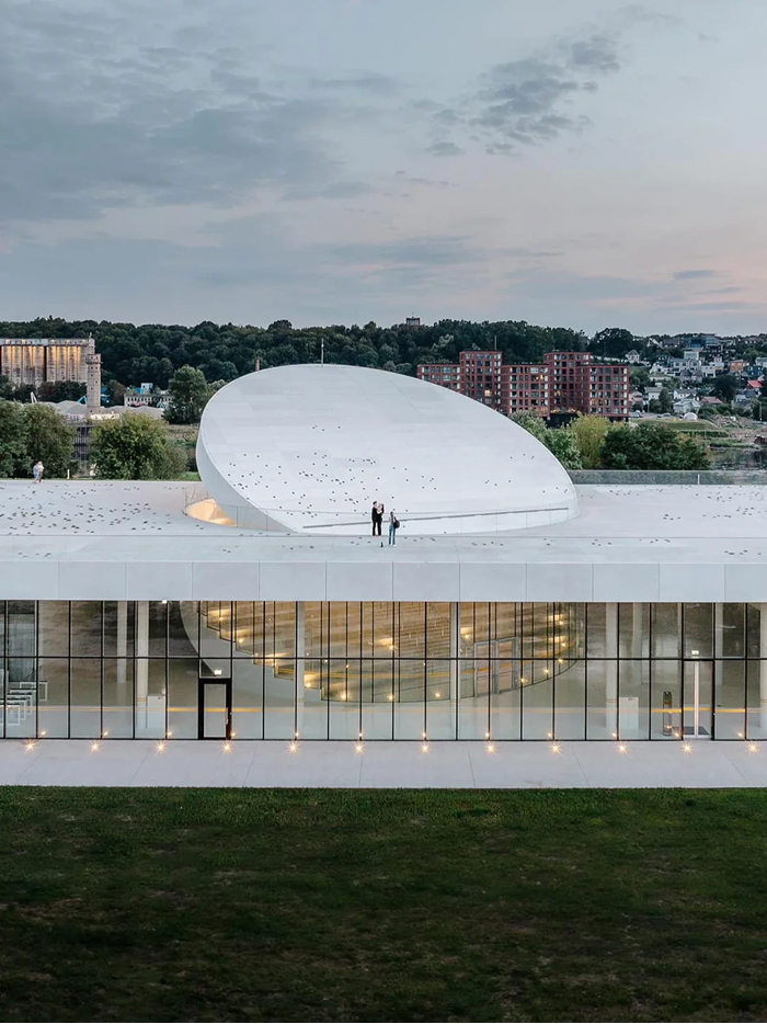 Modern architecture design: A sleek white building with a distinctive, curved roof structure and a transparent facade revealing interior spaces.