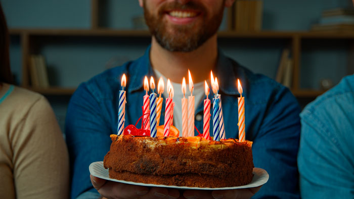 A man holding a birthday cake with lit candles, celebrating a milestone in life, sharing hard truths with others.