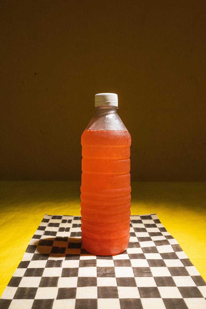 An orange liquid in a plastic bottle on a checkered surface, suggesting unhygienic storage.