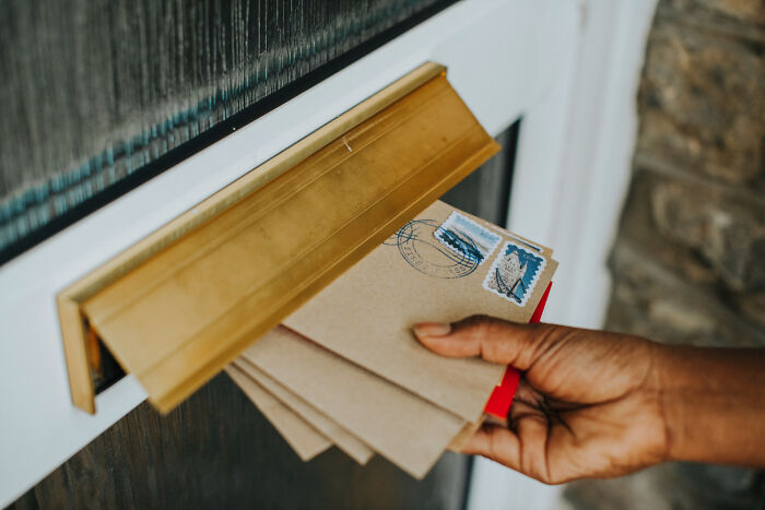 A hand puts brown envelopes with stamps through a gold mail slot. It represents corporate buzzwords and practices.