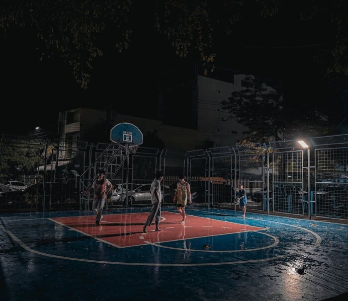 People playing basketball on a wet outdoor court at night, a captivating winning photo from the iPhone Photography Awards.