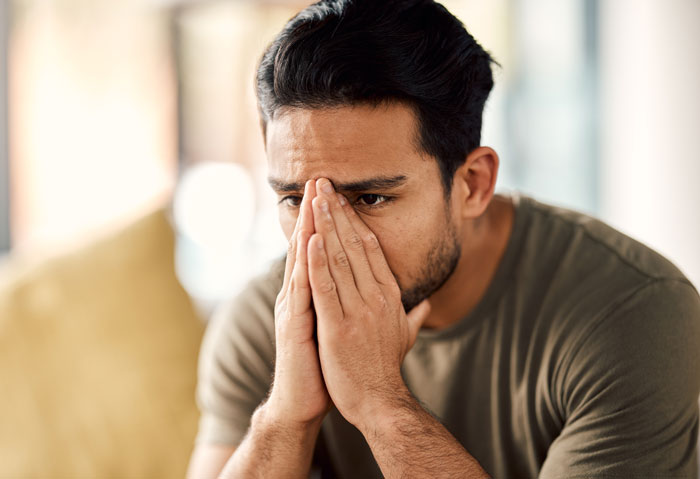 A man looking stressed and holding his face, reflecting the struggles men face after having a baby.